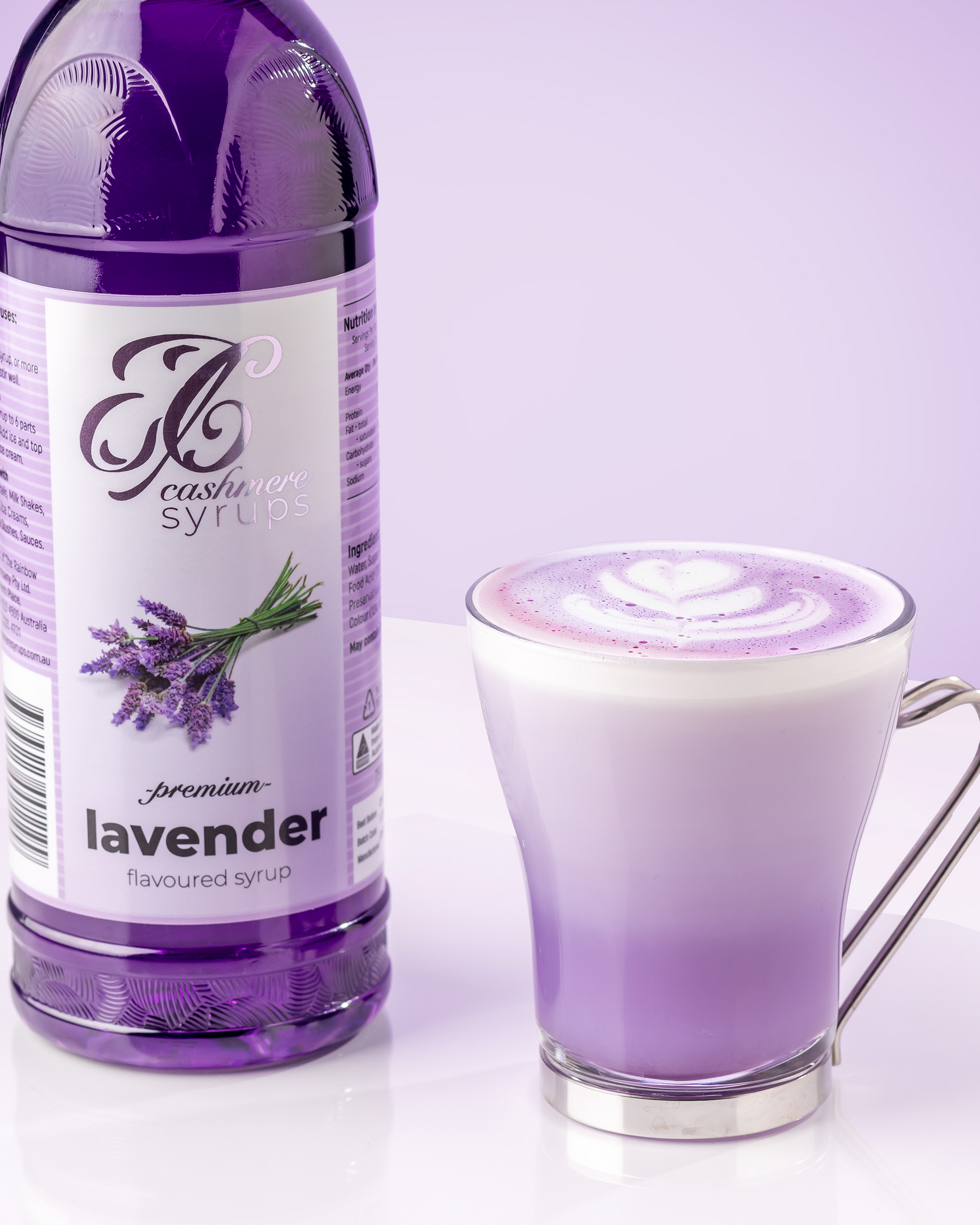 Bottle of lavender syrup next to a frothy lavender coloured drink in a clear glass