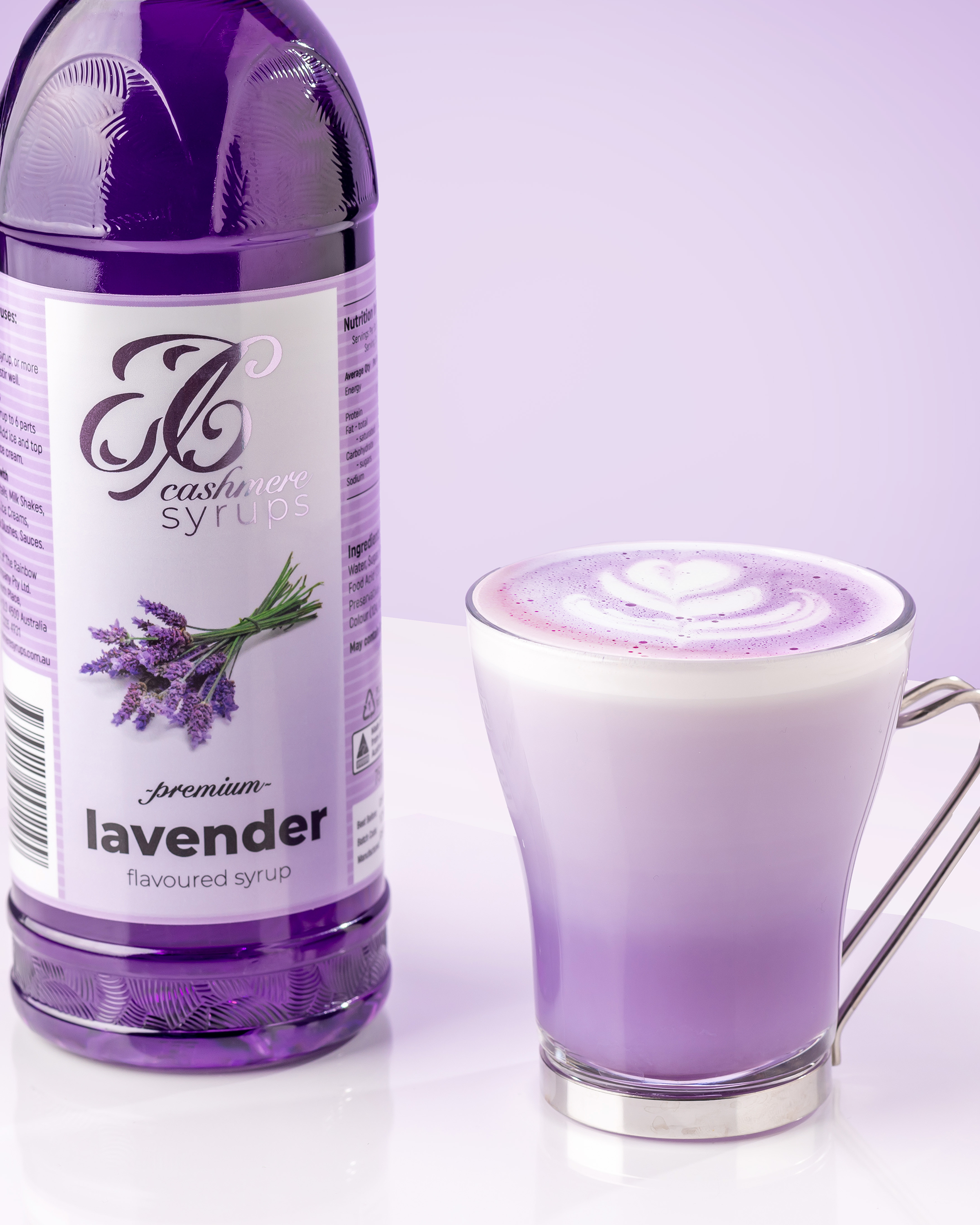 Bottle of lavender syrup next to a frothy lavender coloured drink in a clear glass