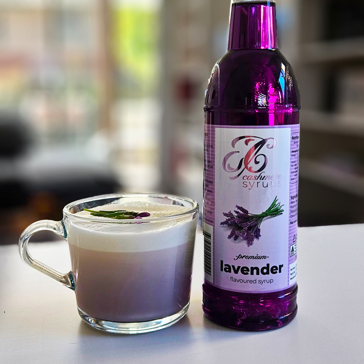 Bottle of Cashmere Syrups Lavender Syrup next to a lavender latte on a kitchen bench